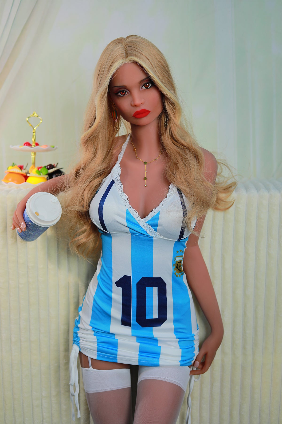 163cm TPE Sex Doll Catherine Medium shot of a doll wearing an Argentina-themed dress and white stockings holding a drinking vessel leaning against a textured white wall