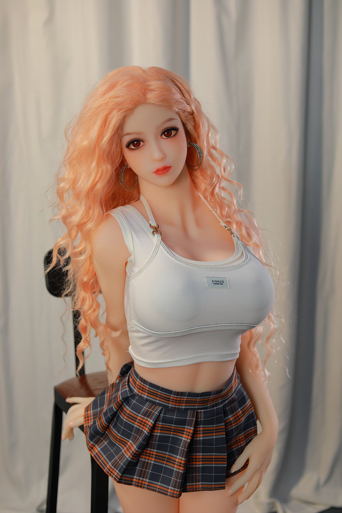 148cm TPE Sex Doll Maya Upper body shot of a doll with peach hair white crop top and plaid skirt standing by a chair against a white curtain