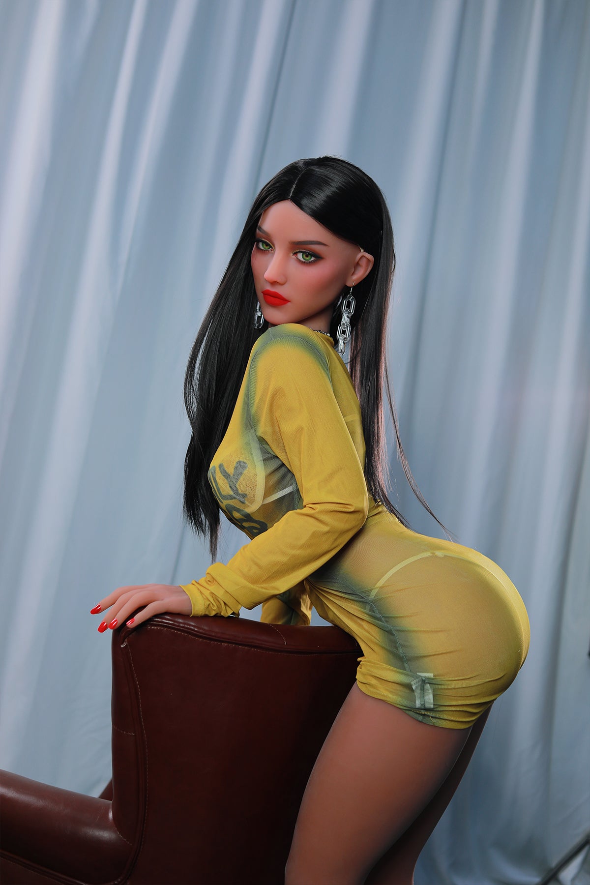 165cm TPE Sex Doll Sienna Side profile of a woman in a sheer yellow dress leaning on a brown leather chair cropped at the knees