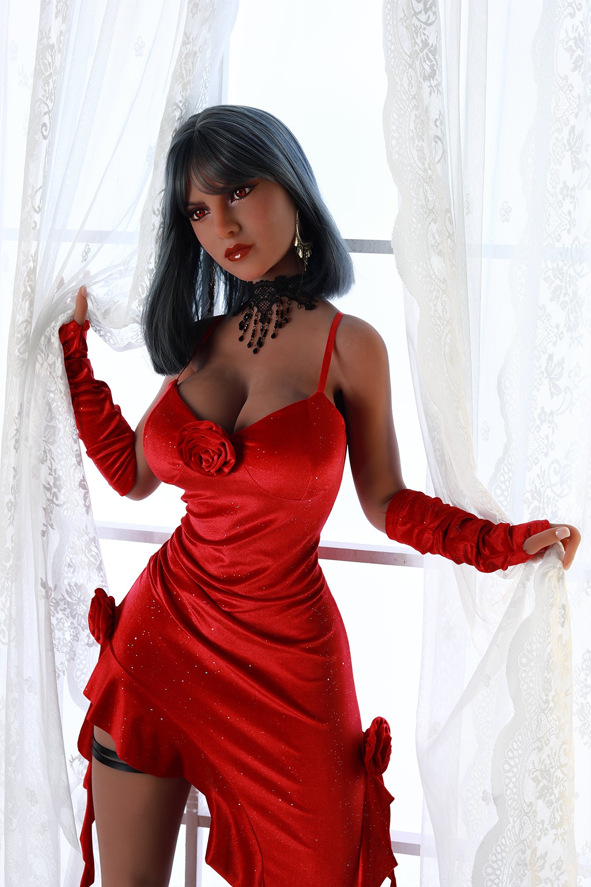 Front view of an adult love doll wearing a red satin mini dress and long gloves standing by white lace curtains