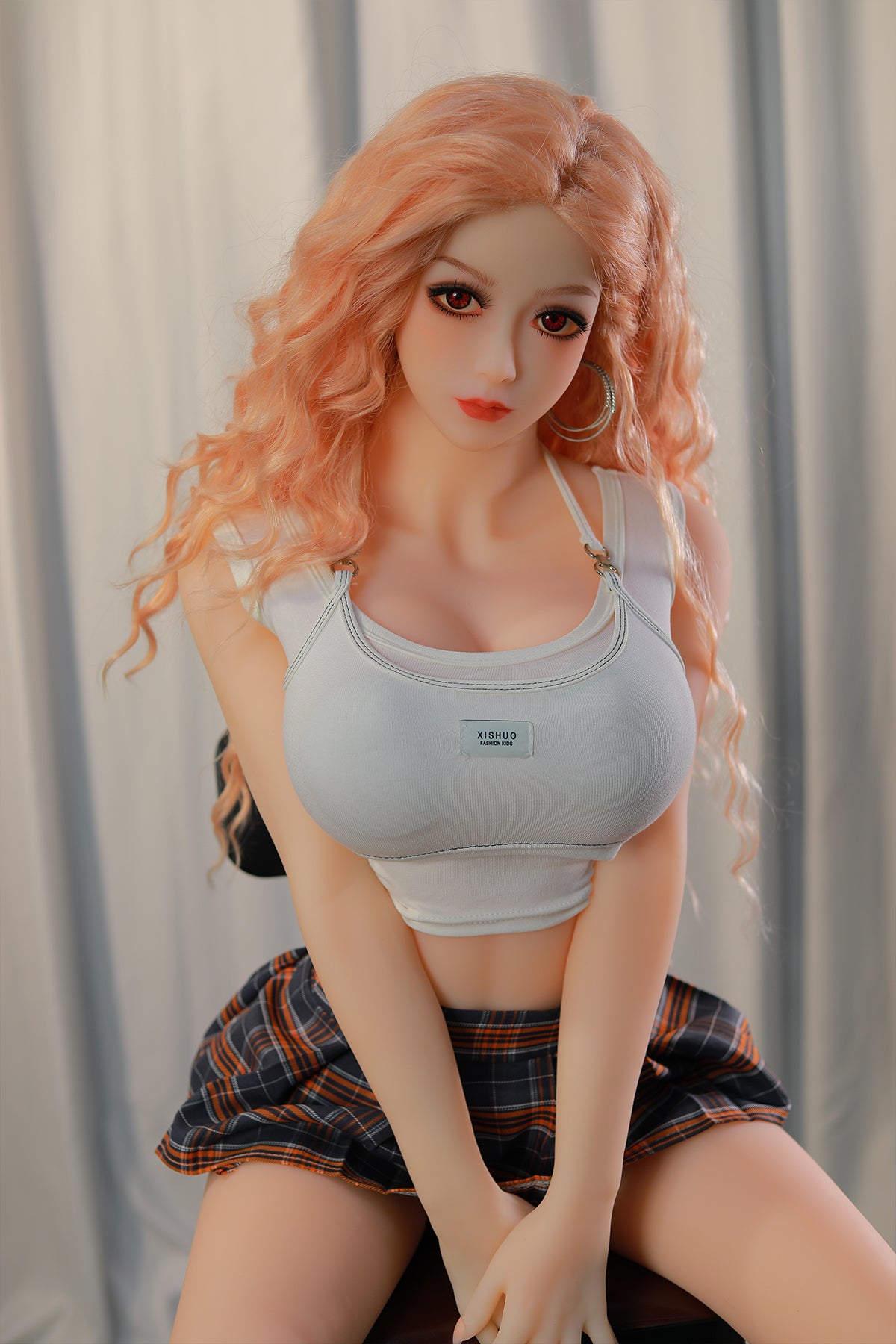 148cm TPE Sex Doll Maya Medium shot of a doll with peach hair white crop top and plaid skirt seated on a chair against a white curtain