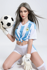 173cm Hybrid Sex Doll Julia A woman with long grey hair wearing a tied Argentina soccer jersey and white shorts holding a soccer ball in one gloved hand while kneeling against a pl